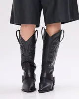 Bota texana de cuero negro con bordados en el caño, punta fina y correa con hebilla metálica.