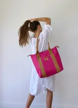 Bolso tipo tote de lona color fucsia con asas de cuero marrón, bolsillo interno y externo.
