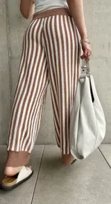 Pantalón tejido a rayas verticales color marrón y blanco, con cintura y tobillos acanalados con cordón ajustable.