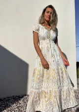 Vestido largo blanco con estampado dorado, escote en V con cordones y mangas cortas abullonadas.