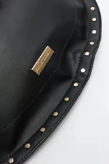 Bolso hobo color beige de símil cuero con textura suave y tachas metálicas en los bordes. Tiene correa al hombro y logo metálico en el frente.
