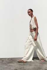 Pantalón blanco de tiro alto con pinzas delanteras, bolsillos laterales y pernera ancha. Cierre lateral con cremallera oculta.