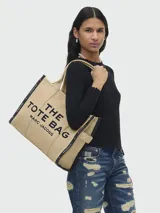 Bolso tote grande Marc Jacobs color beige con estampado del logo de la marca en negro. Tiene doble asa de mano y laterales con inscripción de la marca.