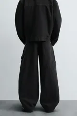 Pantalón negro de corte amplio, confeccionado en tejido de algodón con efecto lavado. Presenta bolsillos frontales, traseros de parche, tira multifunción y bolsillos laterales en las perneras. Cuenta con cierre frontal con cremallera y botón.