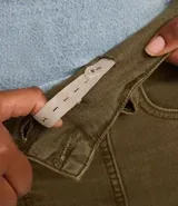 Pantalón flare de sarga color verde oliva, con cintura ancha, doble botón, cierre tradicional, trabillas, detalle de recortes y bolsillos.