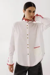 Camisa blanca de poplin con cuello mao, manga larga y cierre frontal con botones. Presenta detalles de crochet rojo en cuello, puños y bolsillo.