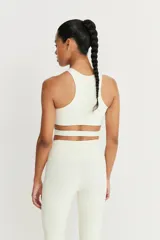 Top deportivo color crudo con tirantes anchos y detalle de tira cruzada en la cintura.