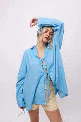 Camisa blanca de lino y algodón, con cuello clásico, cierre frontal con lazos y mangas largas abullonadas con puños ajustables con lazos.