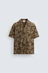 Camisa marrón con estampado floral, corte relaxed fit, cuello bowling, manga corta, bolsillo en el pecho, aberturas laterales y cierre con botones.