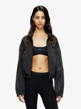 Sujetador deportivo negro, corte crop top, con banda elástica ancha bajo el busto que lleva un logo metálico en el centro.