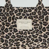 Bolso shopper con estampado de leopardo en tonos beige y negro, con asas cortas y etiqueta con texto en el frente.