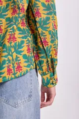Blusa de manga larga con estampado floral en tonos mostaza, verde y rosa. Tiene cuello redondo con lazo ajustable.