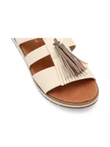 Sandalia de cuero color crema, con tiras cruzadas y detalle de flecos marrones en la parte delantera.