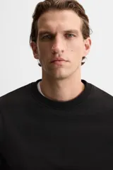 Sudadera negra de corte holgado, cuello redondo y mangas largas con puños acanalados.