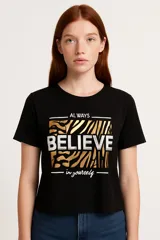 Remera negra de corte clásico con estampado frontal que incluye la frase "Always believe in yourself" sobre un fondo con diseño de cebra en tonos dorados y blancos.