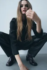 Pantalón de cuero negro de tiro medio, con pinzas delanteras, bolsillos laterales ocultos y corte holgado.
