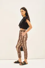 Pantalón estilo babucha con estampado de piel de serpiente en tonos marrones y beige. Posee cintura elástica con cordón de ajuste, puños ajustables en los tobillos y detalles metálicos.
