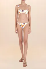 Calzón de bikini de cobertura sutil, color blanco hueso, con estampado abstracto en tonos naranja, azul y rosado. Presenta costuras invisibles y detalles dorados en los laterales.