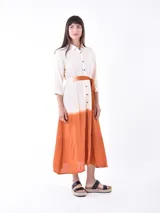 Vestido midi color crudo con efecto degradado color naranja en la parte inferior. Tiene corte camisero, cuello clásico, mangas 3/4 y cinturón de tela color naranja.