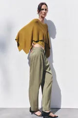 Pantalón color verde oliva de tiro medio con cintura con trabillas, bolsillos laterales, pinzas delanteras y raya planchada. Cierre frontal con cremallera, botón y ganchos metálicos.