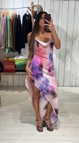 Vestido largo de crepé con estampado floral en tonos rosados, morados y blancos. Presenta escote buche con drapeado y espalda baja ajustable con tiras finas. El ruedo es irregular, más corto en el frente.