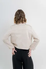 Chaqueta color beige de tela tipo gamuza con elastano, cuello solapa, manga larga con trabillas en hombro, bolsillos delanteros con cremallera metálica y cierre frontal con cremallera.
