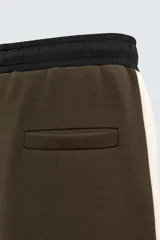 Pantalón jogger color verde oliva, corte relaxed fit, con cintura elástica ajustable con cordón, bolsillos laterales y detalle de bolsillo de vivo en la espalda. Presenta una banda lateral color crema a contraste.