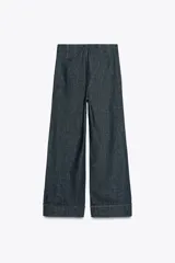Pantalón culotte de tiro alto en denim azul oscuro, con pernera ancha y corta terminada en vuelta. Presenta falsos botones dorados en la parte delantera, bolsillos frontales y cierre con cremallera y gancho.