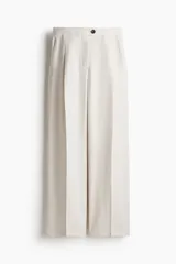 Pantalón sastrero color beige de sarga con pinzas, corte holgado, tiro alto, pretina prolongada con botón, bolsillos al bies y bolsillos insertados atrás. Piernas anchas con pliegues adelante y atrás.
