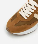 Championes de estilo jogging para mujer, confeccionados en poliuretano color tostado con recortes contrastantes en color crema. Presentan cierre de cordones blancos y suela de PVC que se extiende hasta el talón con base dentada.