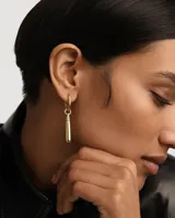 Aro individual dorado con forma de argolla y dije colgante en forma de gota.