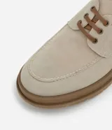 Zapato estilo dockside de color beige claro, confeccionado en gamuza sintética, con cordones marrones y suela track gruesa de goma color marrón. Presenta costuras visibles en la puntera y ojales metálicos para los cordones.