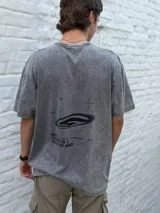 Remera gris oscuro con efecto acid wash, corte oversize y manga corta. Presenta un estampado minimalista en negro con texto que incluye "TRUTH IS A STATE OF MIND" y un logo gráfico.