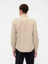 Camisa de manga larga color beige, de corte clásico, con cuello abotonado, bolsillo en el pecho y logo de oso bordado.