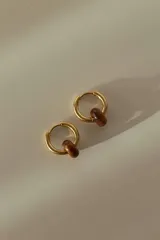 Par de aros tipo argolla dorados con dije de piedra natural con patrón de manchas negras sobre fondo blanco.