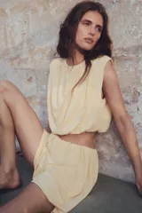 Top cropped color crema, sin mangas, de punto suave con costuras fruncidas para una silueta abullonada con efecto drapeado.