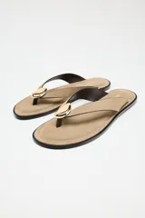 Sandalia plana color beige, con tira de serraje para el dedo y adorno metálico dorado.