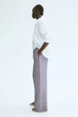 Pantalón recto de tela vaporosa a rayas verticales blancas sobre fondo gris. Tiene corte holgado, cintura elástica con cordón de ajuste, bolsillos laterales y traseros insertados.