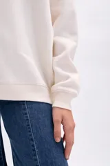 Buzo de algodón color crudo con cuello redondo y manga larga. Presenta bordado frontal en color verde que dice "Wellness Club Body. Mind. Balance Since 1994".