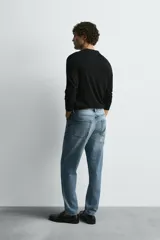 Jeans de denim de algodón, color negro lavado, con tiro medio, corte ajustado en cadera y muslos, y pierna que se estrecha hacia el tobillo. Presenta cinco bolsillos y cierre frontal con cremallera y botón.