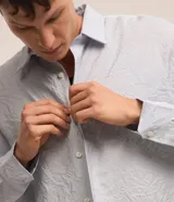 Camisa celeste de viscosa y poliéster con textura arrugada, cuello tradicional, manga larga y abotonadura frontal completa.