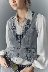 Chaleco de denim rígido lavado a gris claro, con botones metálicos grabados, bolsillos con solapa en el frente y tira de ajuste en la espalda. Presenta detalles de pasacintos en el escote.