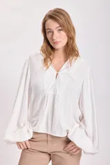 Blusa blanca de mangas largas abullonadas con cuello en V y detalle de botón en el frente.