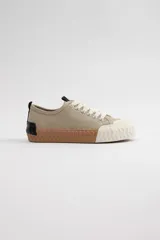 Zapatillas acordonadas color beige con suela marrón y puntera blanca.