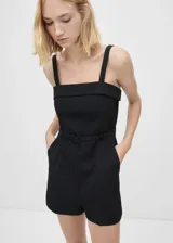 Mono corto negro de tejido mezcla de lana con tirantes anchos, cuello escotado, trabillas y cinturón decorativo. Presenta dos bolsillos laterales, diseño recto y cierre de cremallera invisible en la parte posterior.