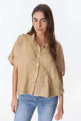Camisa color beige de lino con cuello camisero, manga corta y cierre frontal con botones. Presenta detalles de encaje en el cuello, el frente y las mangas.
