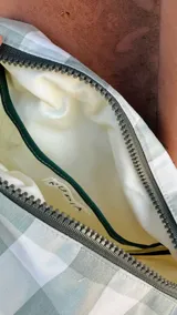 Necessaire rectangular de tela estampada a cuadros verdes y blancos, con cierre superior y etiqueta verde con logo.