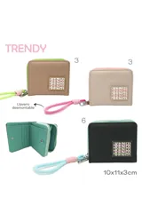 Billetera pequeña tipo monedero con cierre de cremallera, color beige claro con ribetes rosados. Presenta un parche frontal con el texto 'TRENDY' repetido en bloques de color rosa y blanco. Incluye una correa de mano trenzada en tonos rosa y blanco atada al tirador de la cremallera.