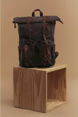 Mochila marrón de lona con detalles en cuero, cierre superior enrollable con hebillas y dos bolsillos frontales con hebilla.