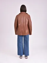 Chaqueta negra de cuero sintético, con cuello clásico, solapas y cierre frontal con un botón.